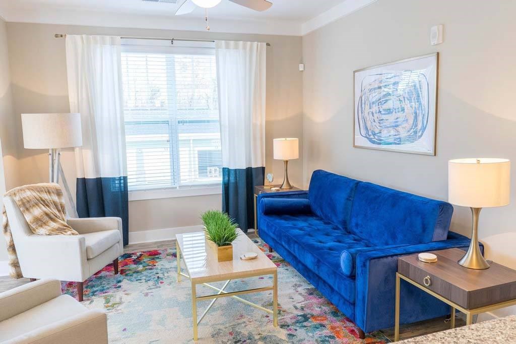 A blue couch sits in a living room with a white chair and a small table with a plant on it at Foxwood Apartments, North Carolina