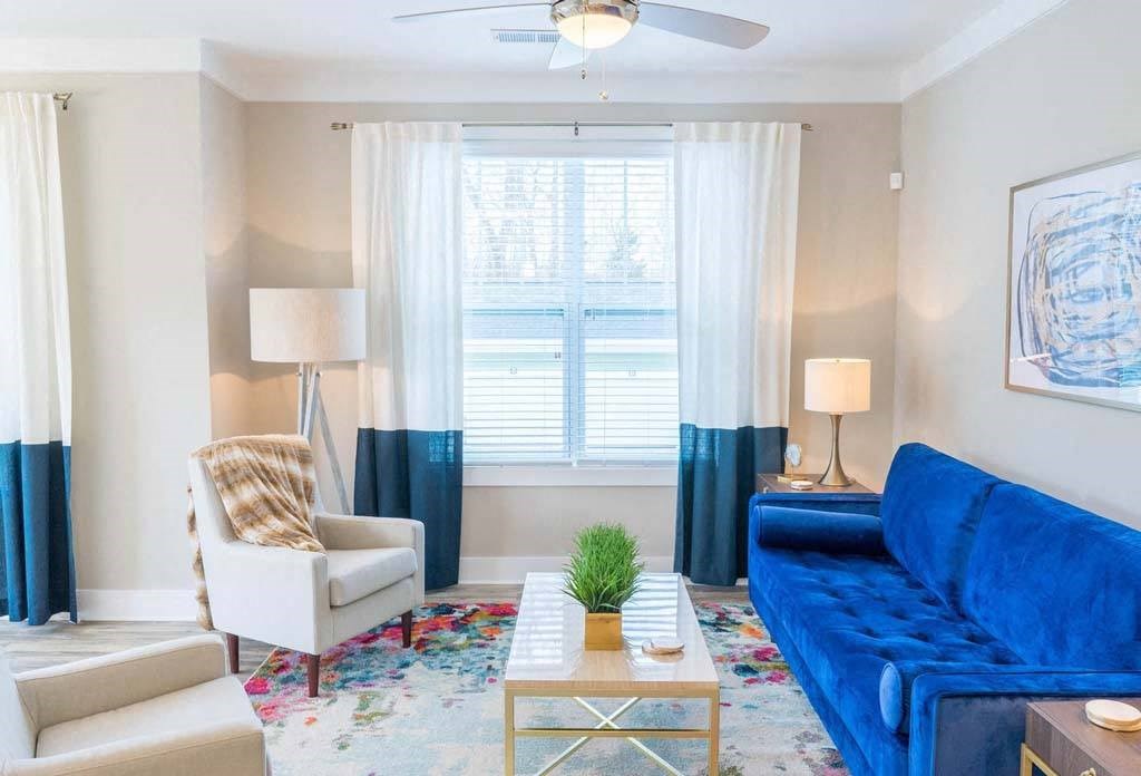 A living room with a blue couch, a white chair, and a small table with a plant on it. at Foxwood Apartments, Raleigh-Durham