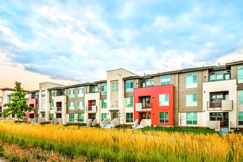 A row of modern apartment buildings with a grassy field in the foreground.