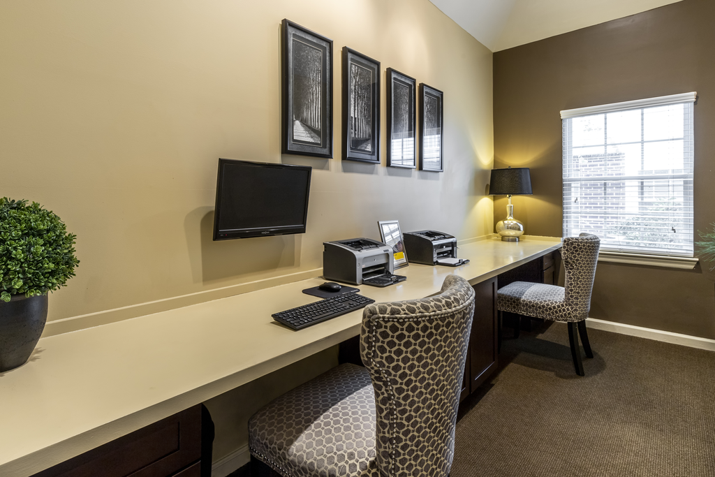Business center with long white desk, two computers, two chairs, and printers, with wall art