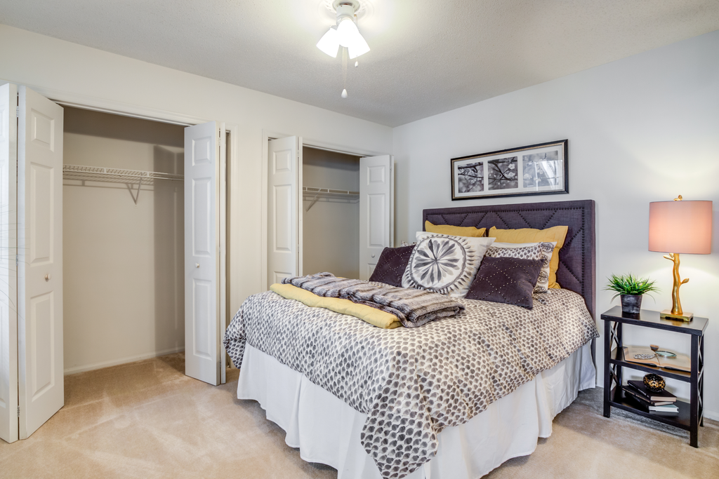 Staged living room with whit walls, large window with decorative curtains, carpeted floors, couch and coffee table, wall art, and entry table next to front door.