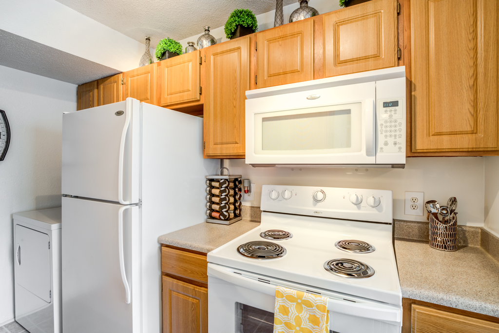 Staged kitchen with white appliances, wood cabinetry, granite style counter tops, and full-size dryer in the background.