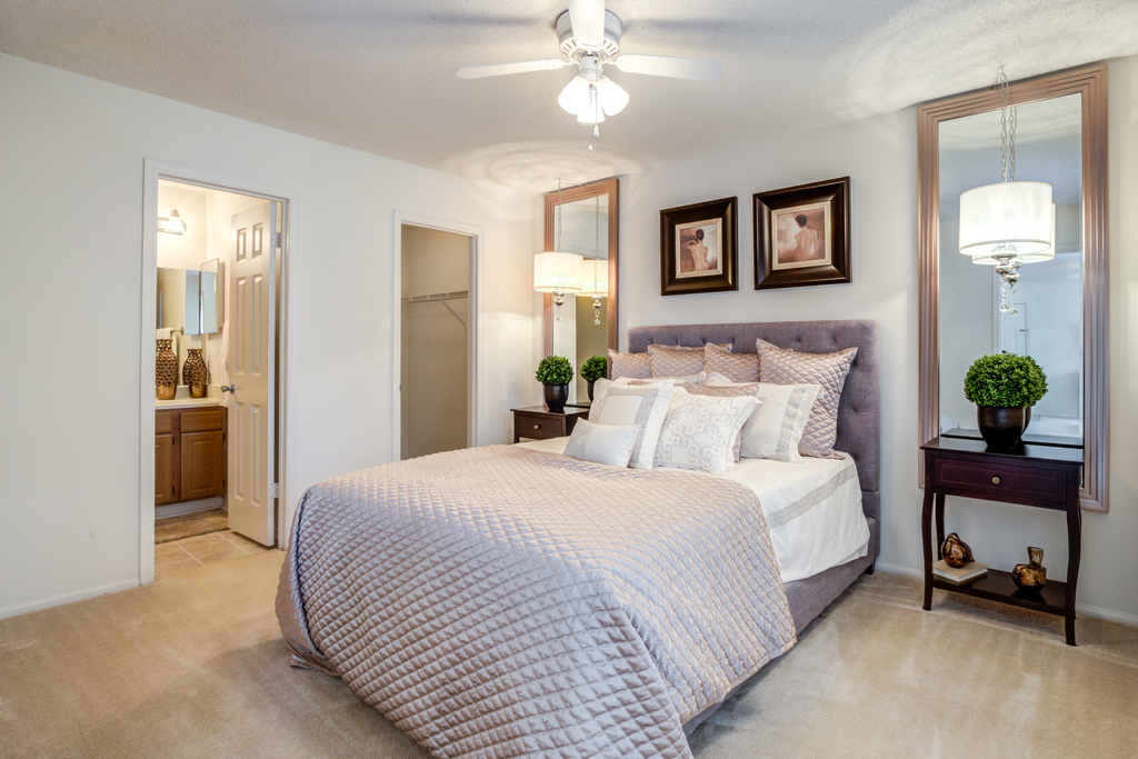 Staged living room with whit walls, large window with decorative curtains, carpeted floors, couch and coffee table, wall art, and entry table next to front door.
