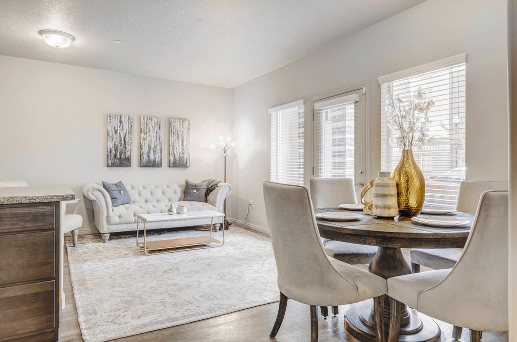 A dining room with a white sofa, a table with chairs and a vase.