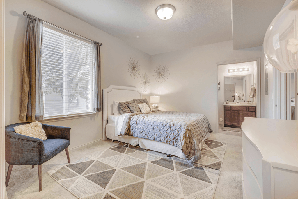 A bedroom with a bed, chair, and window.