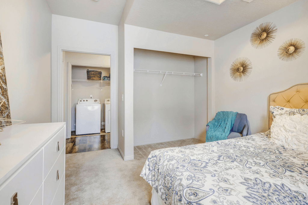 Virtually staged bedroom with carpet, closet, white dresser, blue chair overlooking closet and laundry area in hall way