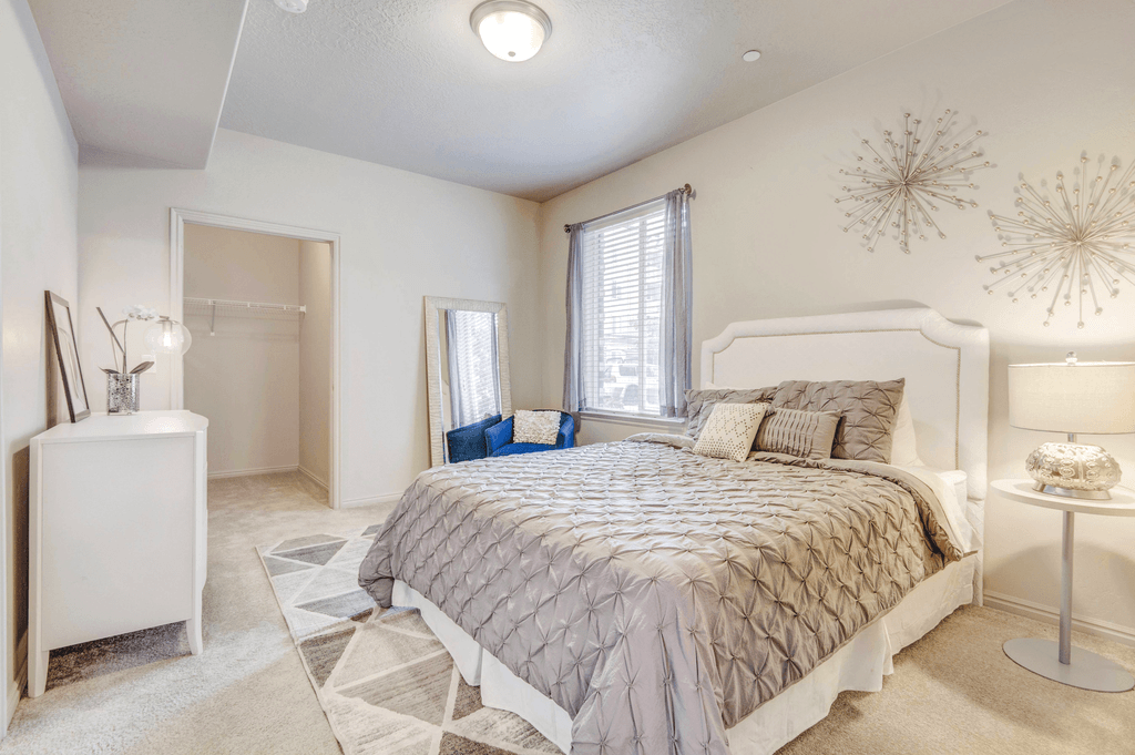 Virtually staged bedroom with carpet, accent run, walk in closet, window with blinds and curtains and white dresser with blue chair