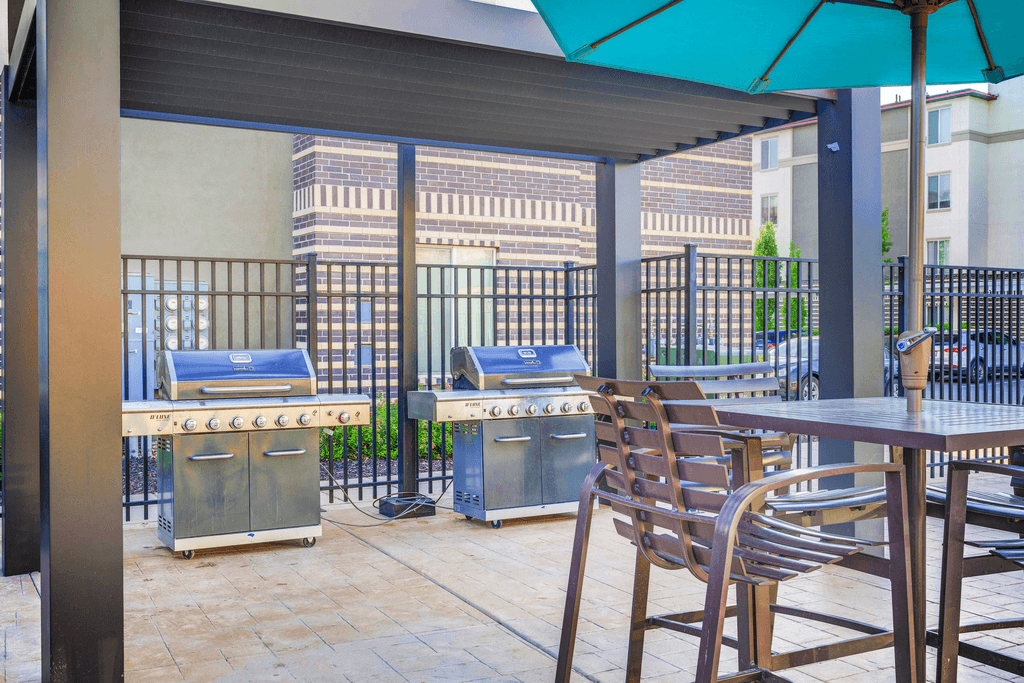 Grill area on pool deck with pergola and tables and chairs with blue umbrellas