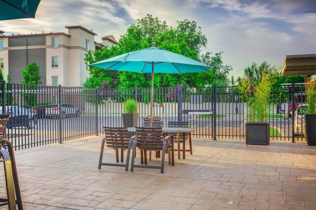 Tables and chairs with blue umbrella on fenced in pool tanning deck
