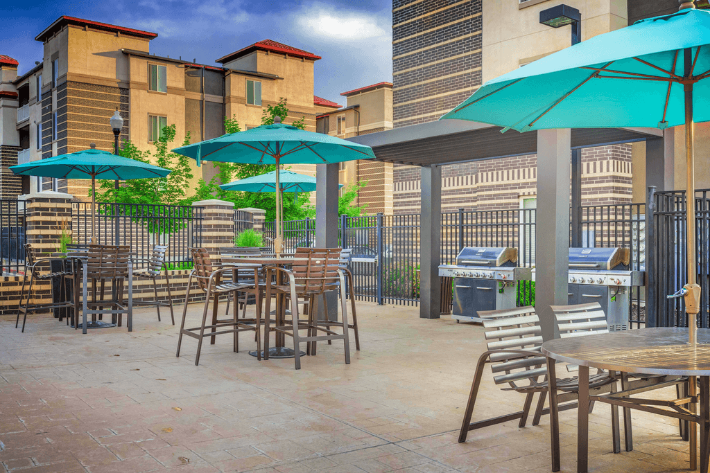 Pool deck  and grill area with pergola, tables and chairs with blue umbrellas and native surrounding landscape and building exterior