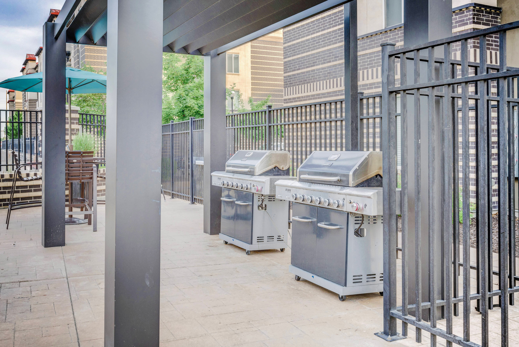 Fenced in grill area with pergola and tables and chairs with blue umbrella