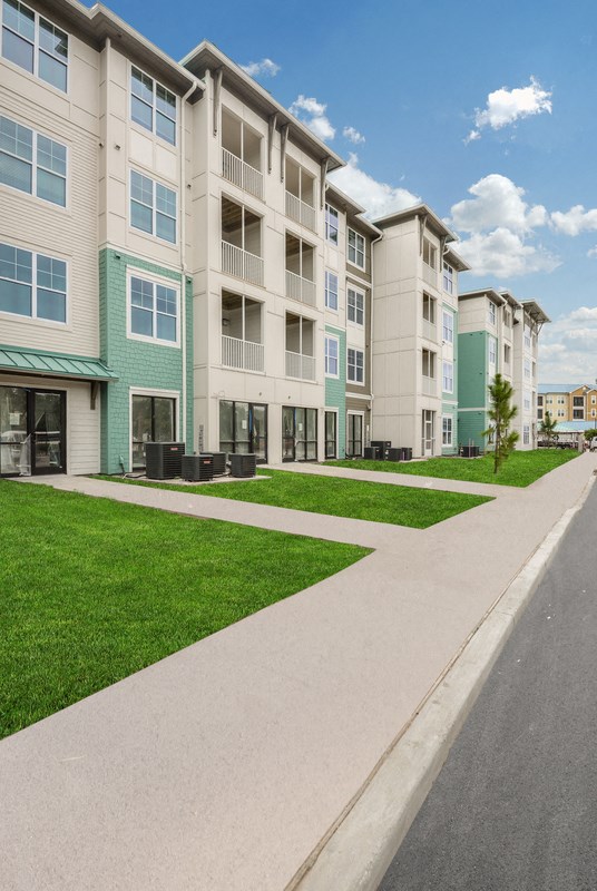 a row of new apartment buildings with green grass and a sidewalk