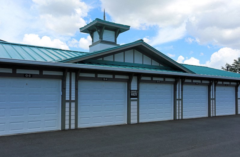 a row of white garage doors on a building with a green roof