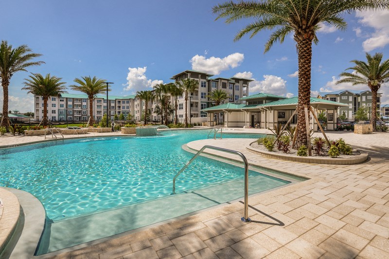 a swimming pool with palm trees and apartments in the background