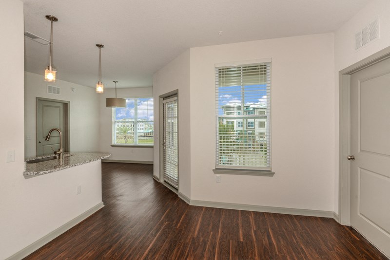 an empty living room and kitchen with hard wood flooring and white walls