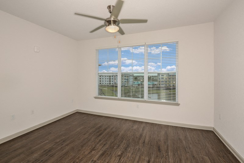 an empty living room with a large window and a ceiling fan