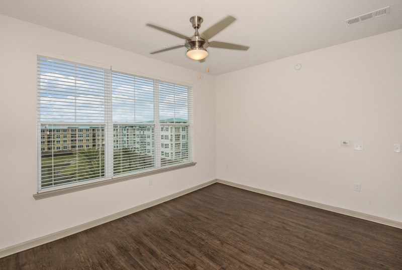 the living room of an apartment with a large window and a ceiling fan