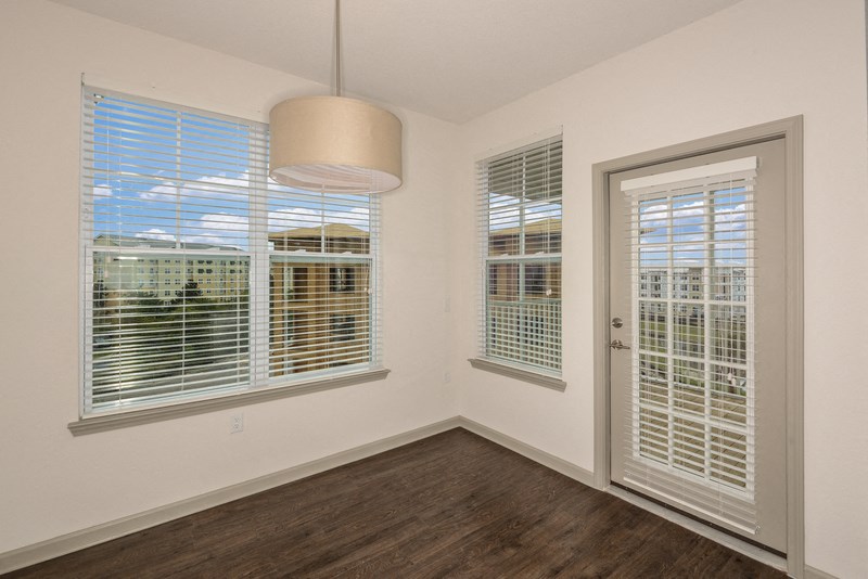 the living room of an apartment with wood flooring and large windows