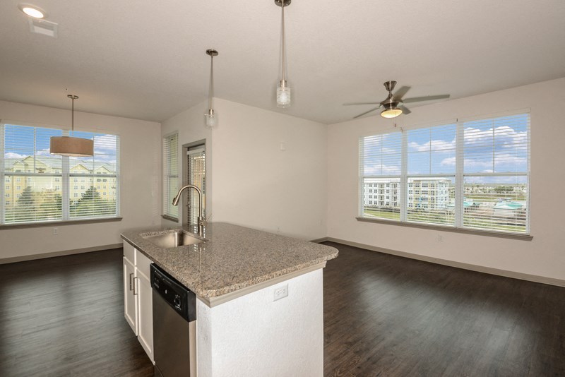 an empty living room with a kitchen with a granite counter top