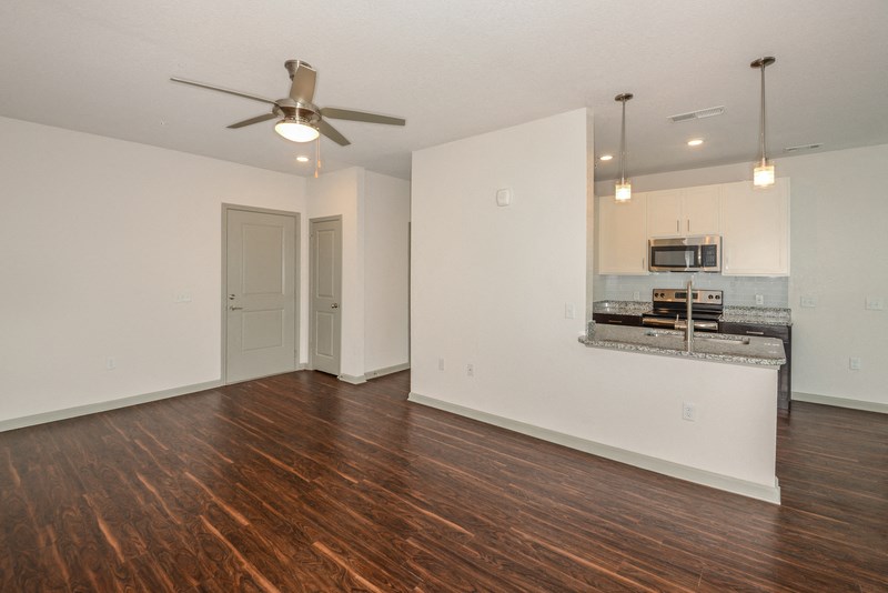 an empty living room with a ceiling fan and a kitchen