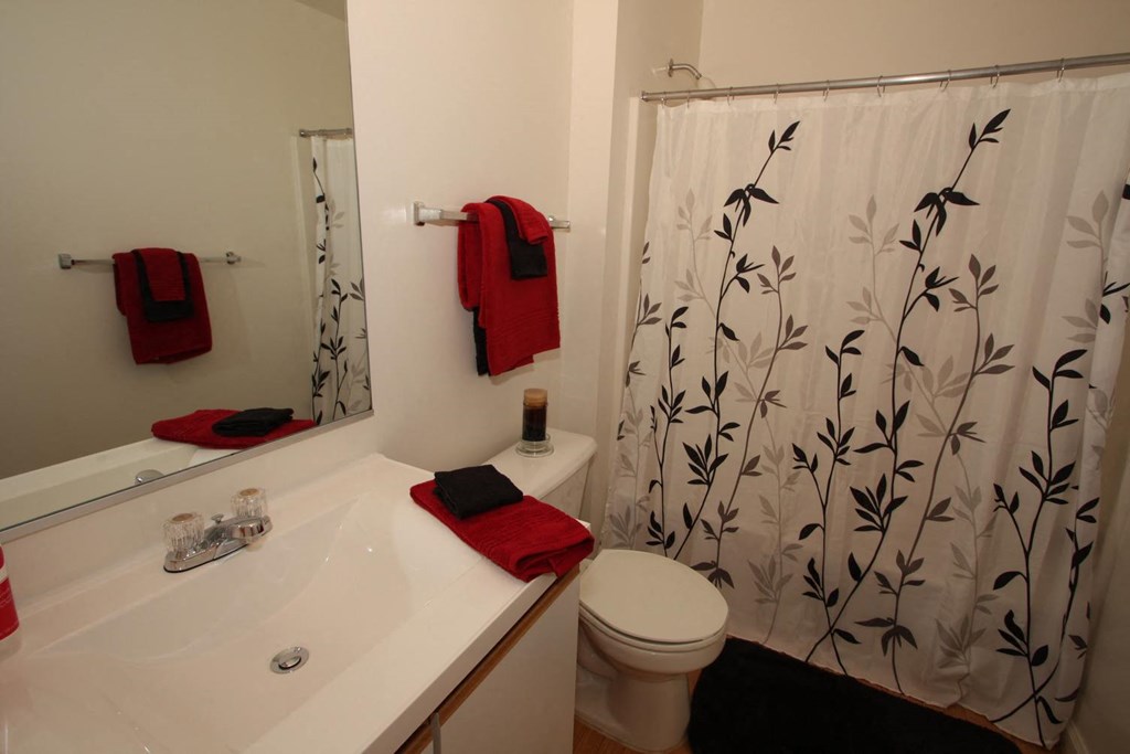 Bathroom with shower curtain and sink with white counter top and red towels hung up