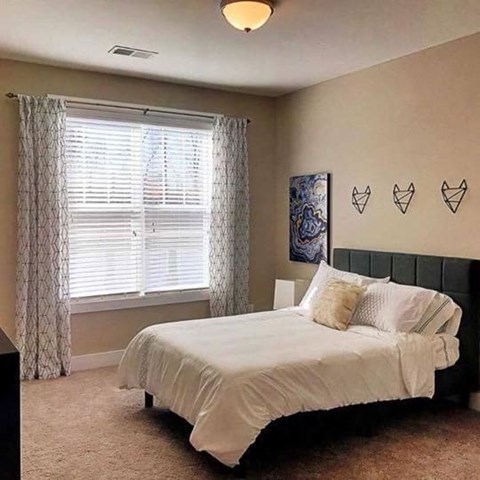A bedroom with a bed, pillows, and a window with curtains.