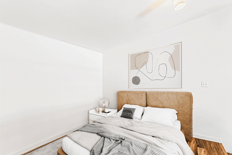 A bedroom with a bed, nightstand, and a painting on the wall.