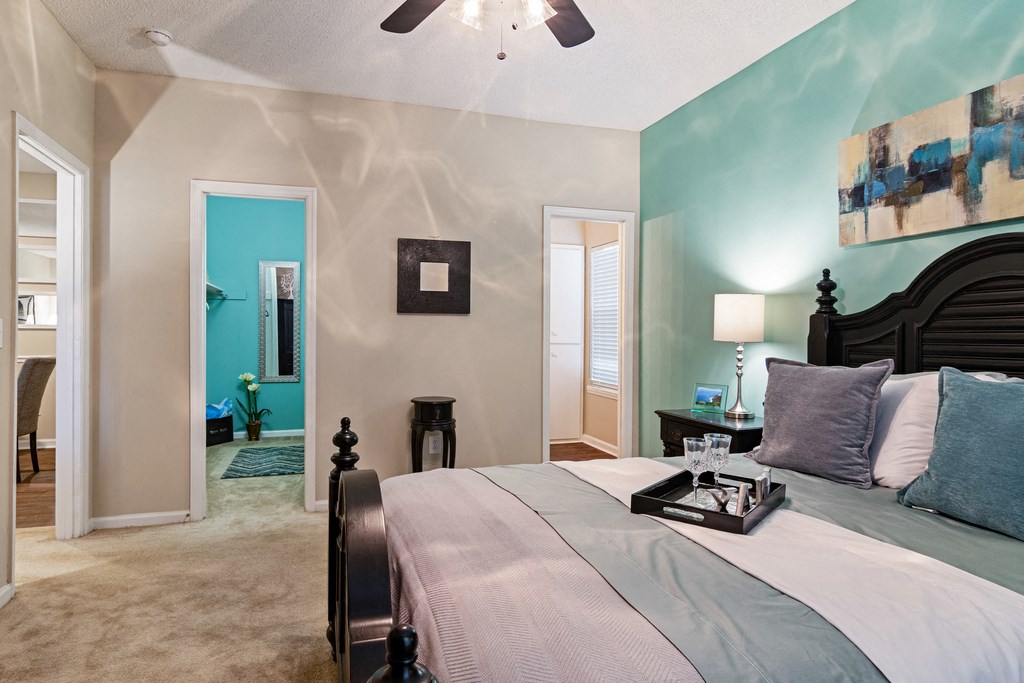 carpeted bedroom with bed, art on the wall and view of bathroom and closet in the background