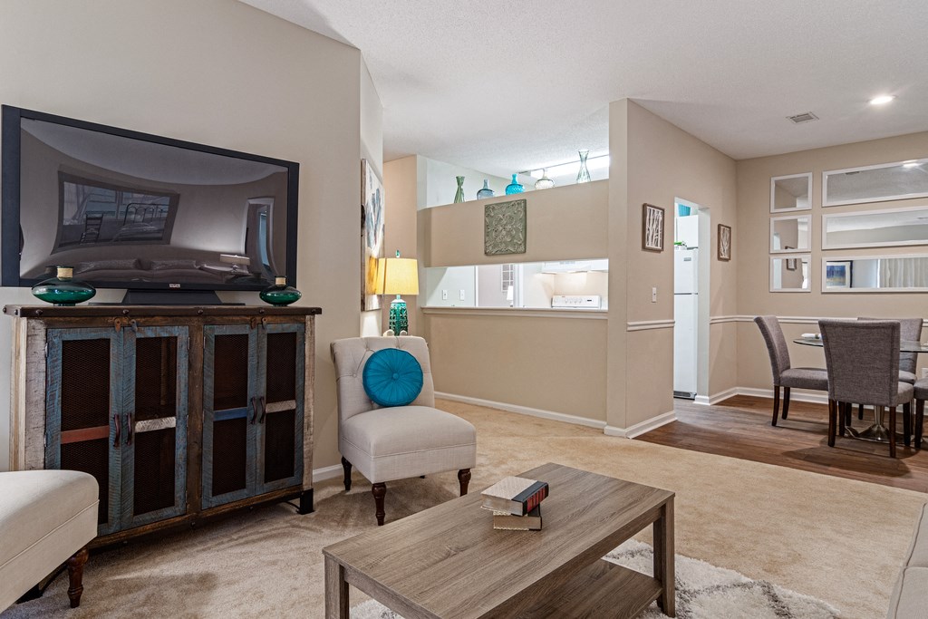 carpeted living room with entertainment center, mounted tv, 2 chairs, and view of dining table and kitchen in the background