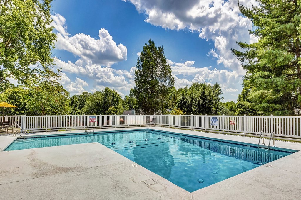 A large outdoor swimming pool surrounded by a white fence and trees. at Brandemere Apartment Homes, North Carolina, 27106