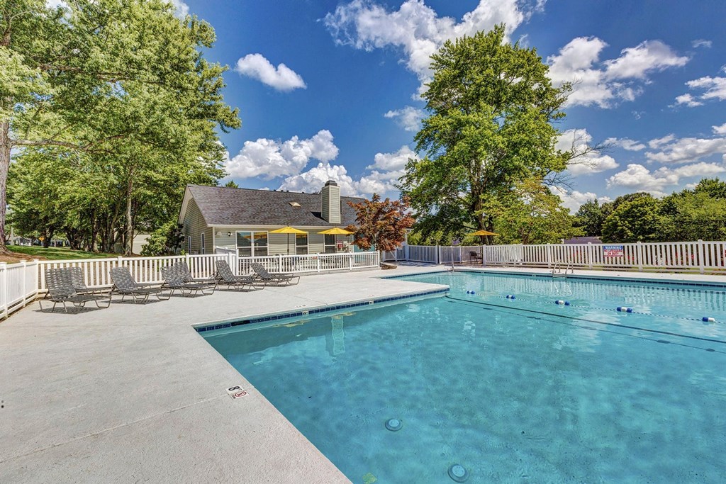 A large swimming pool surrounded by trees and a house in the background. at Brandemere Apartment Homes, North Carolina