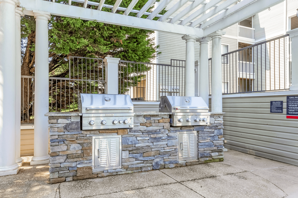 an outdoor kitchen with two grills and a stone wall at Bridges at Mallard Creek Apartment Homes, North Carolina, 28269