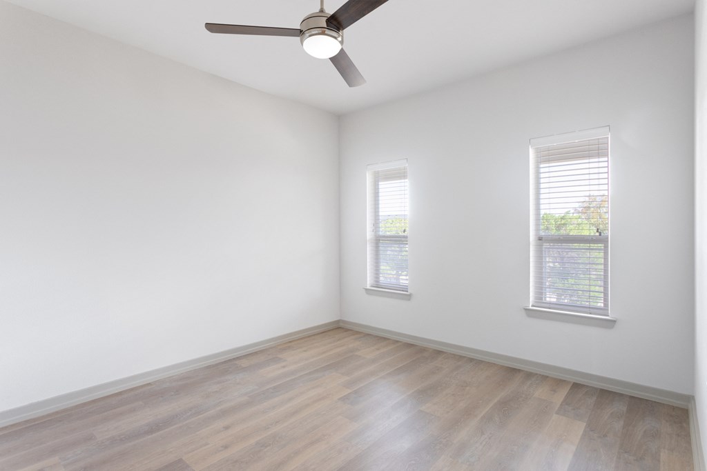 an empty room with a ceiling fan and two windows