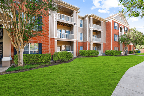 A red brick apartment building with green bushes and trees.