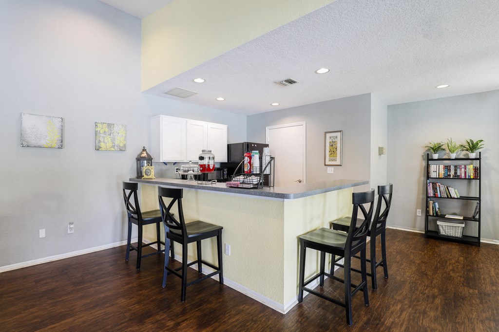 Clubhouse kitchen with white cabinets, grey countertops, breakfast bar with 4 barstools, coffee station and black appliances