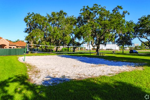 A sandy volleyball court surrounded by trees and a green fence.