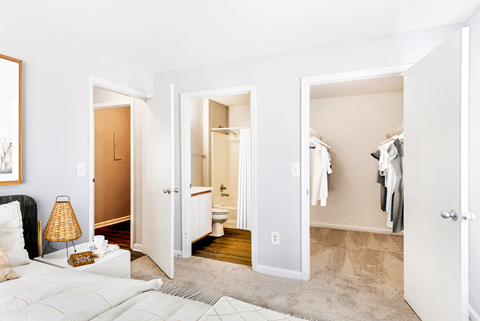 A bedroom with a bed, a nightstand with a lamp, and a closet with clothes.