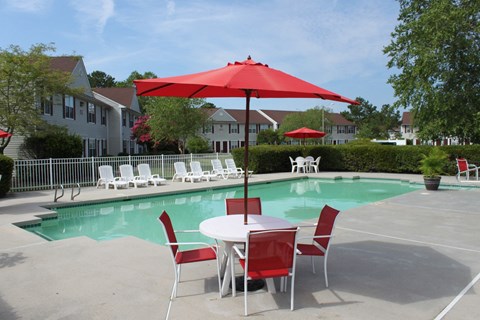 Community swimming pool with four red chairs and a red umbrella surrounding a table