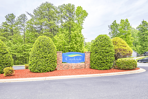 A sign that says "Creekside" is in front of a row of bushes.