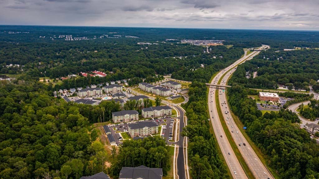 A highway cuts through a wooded area with a large building to the left at Foxwood Apartments, North Carolina, 27616