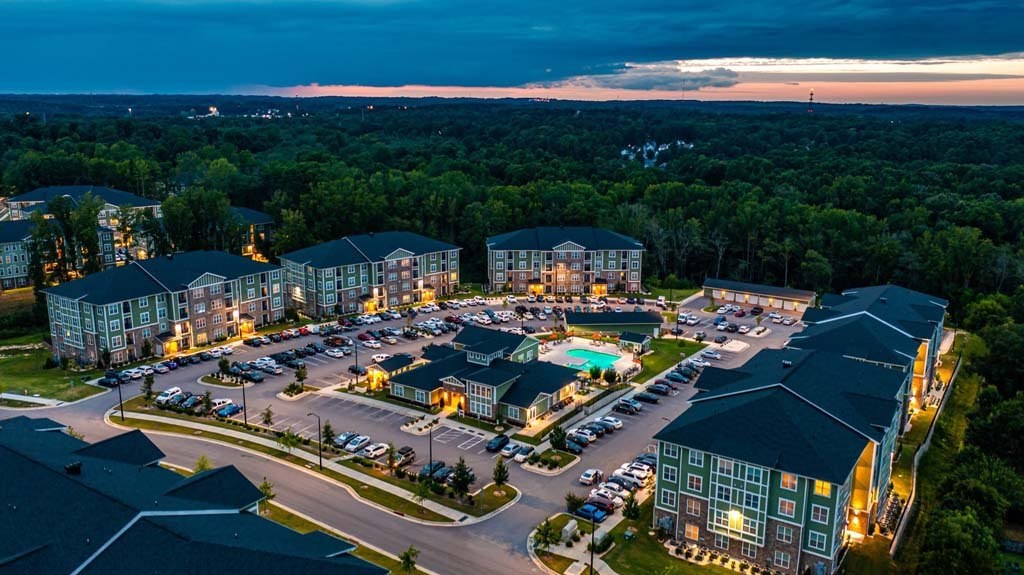 A large, well-lit residential complex at dusk with a parking lot in the foreground. at Foxwood Apartments, North Carolina, 27616