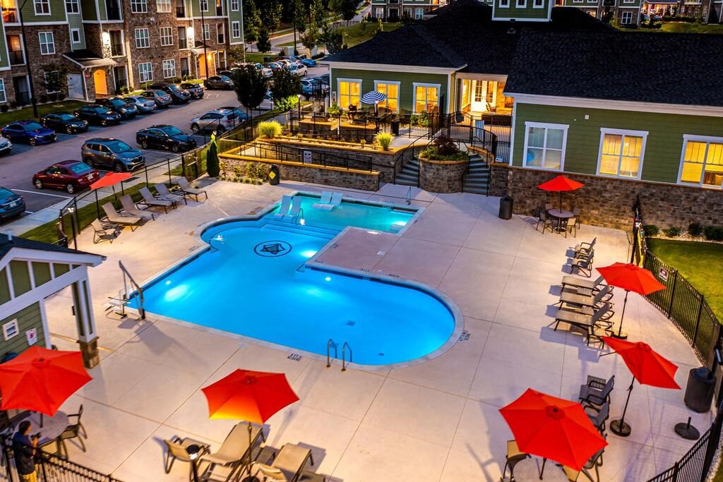 A swimming pool surrounded by red umbrellas and lounge chairs at Foxwood Apartments, Raleigh-Durham