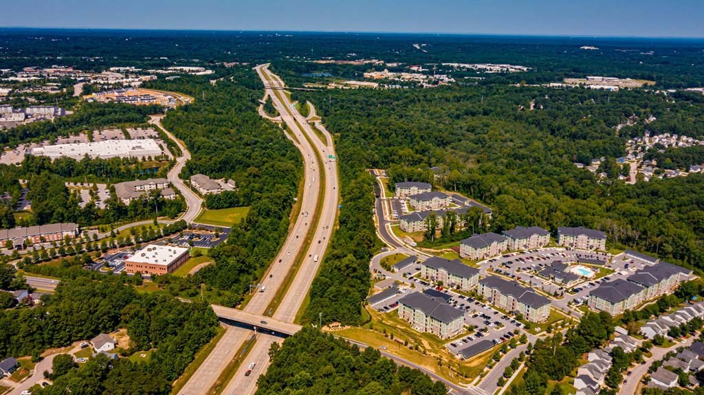 A highway curves through a wooded area with apartment buildings on one side and a parking lot on the other at Foxwood Apartments, North Carolina