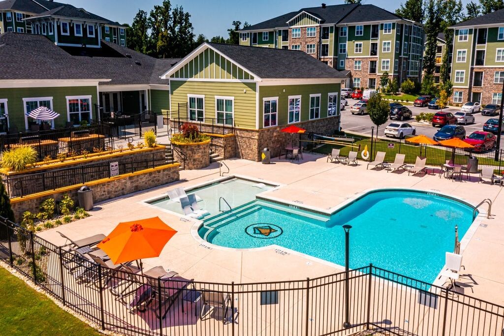 A pool surrounded by a black fence with orange umbrellas at Foxwood Apartments, North Carolina, 27616