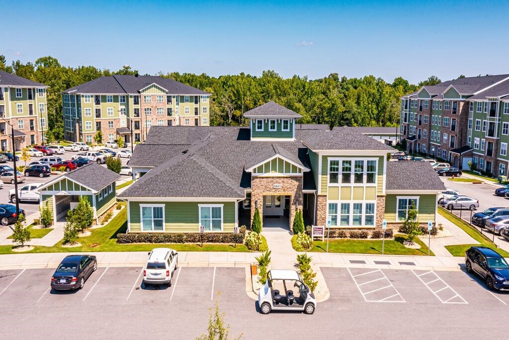 A parking lot with cars and a golf cart in front of a building with a green roof at Foxwood Apartments, North Carolina, 27616