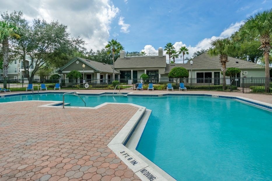 Swimming pool with sundeck, lounge seating, with clubhouse in the background surrounded by landscaping