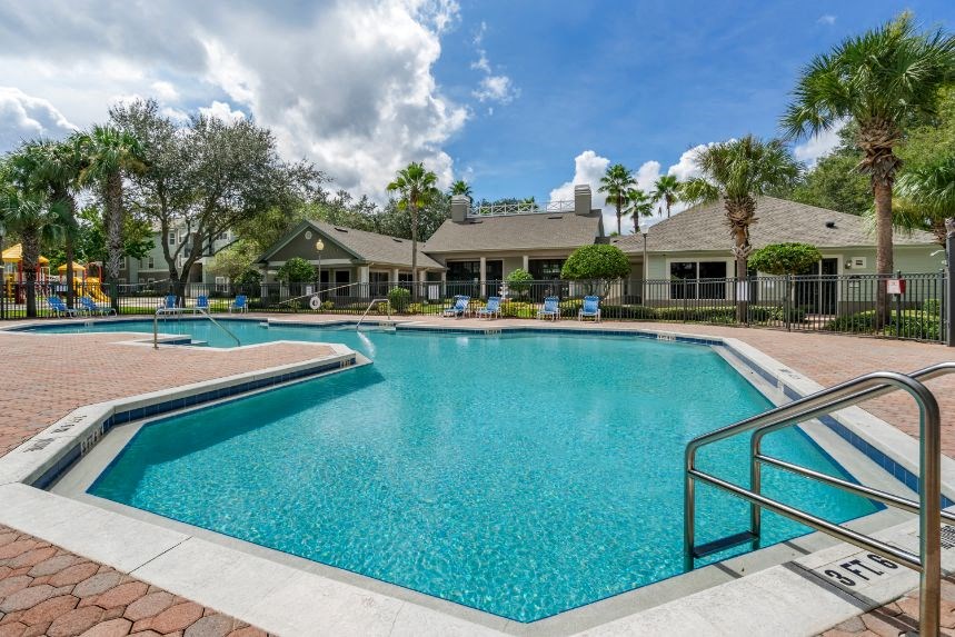 Swimming pool with lounge seating surrounded by native landscaping and clubhouse in the background