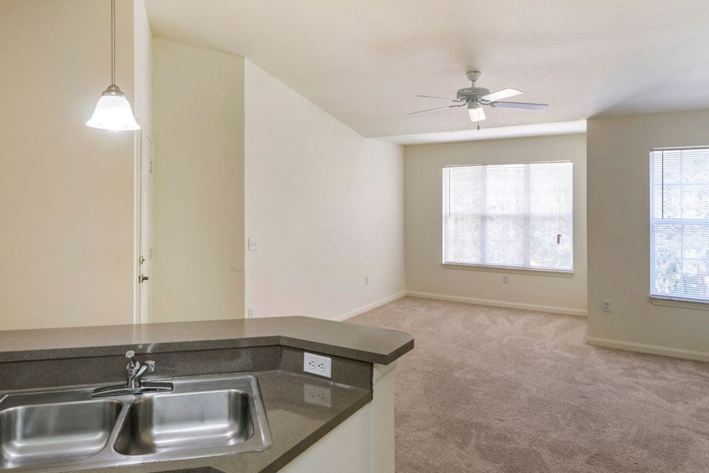 Kitchen breakfast bar overlooking dining room with pendant lighting and living room with carpet flooring and multi speed ceiling fan