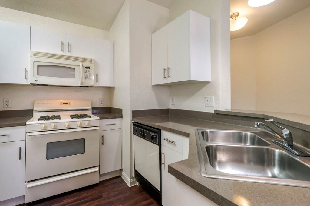 Fully equipped kitchen with white appliances, white cabinetry, and double basin sink