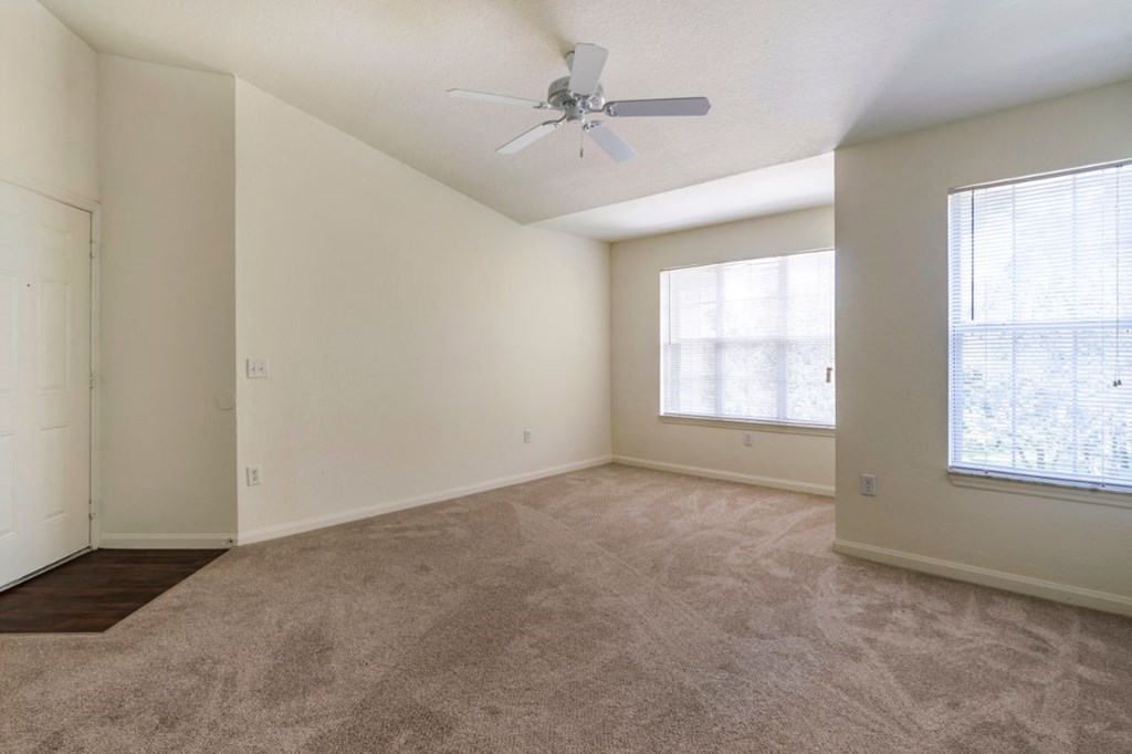 Spacious living room with carpet flooring, ceiling fan, and large windows for natural lighting